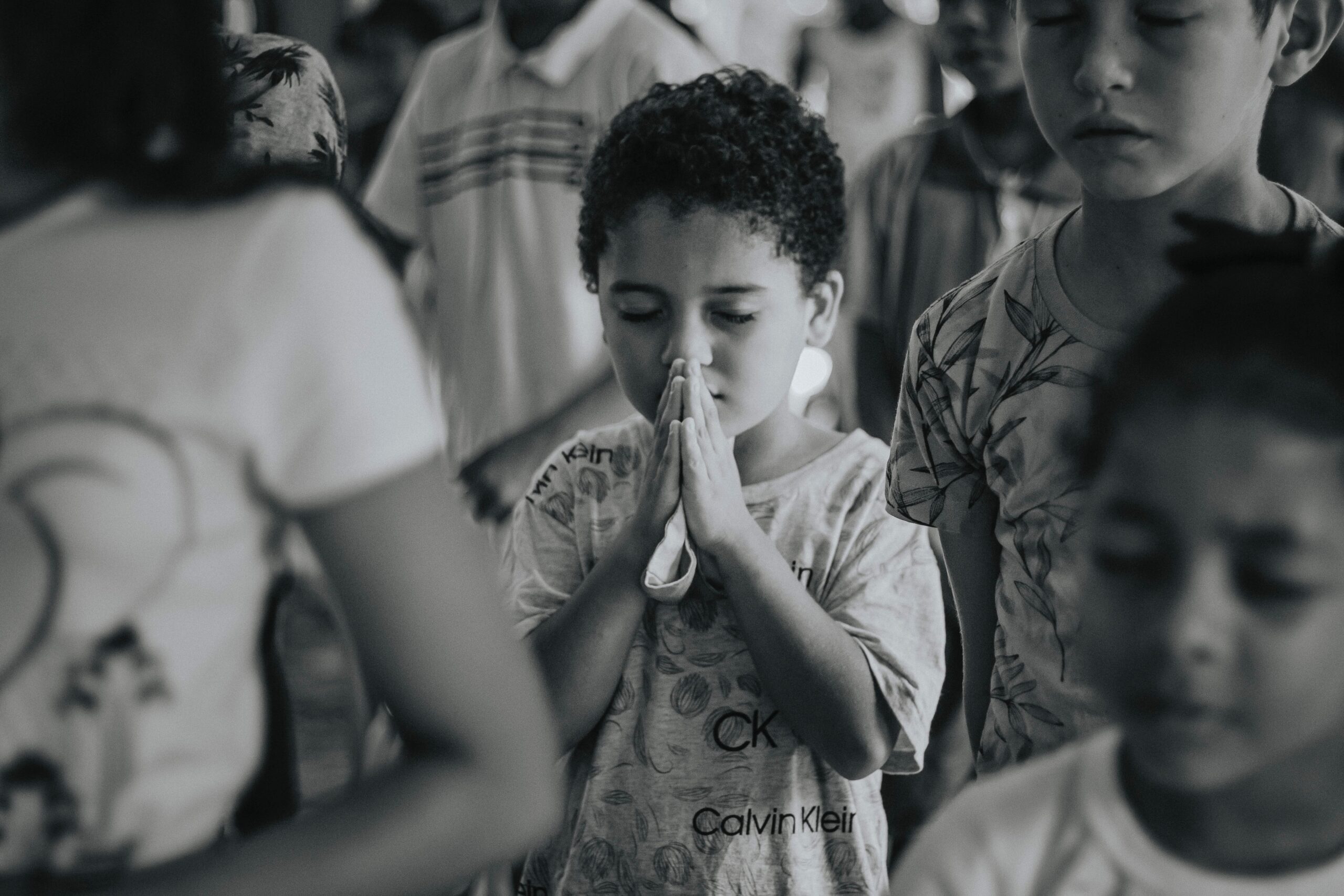 A young boy is praying in the middle of a crowd. Your faith can be tested when you are struggling through various trials. Christian counselors at Sojourner Counseling can help you strengthen your faith as you work through difficulties. Begin your Christian counseling in Raleigh NC today.